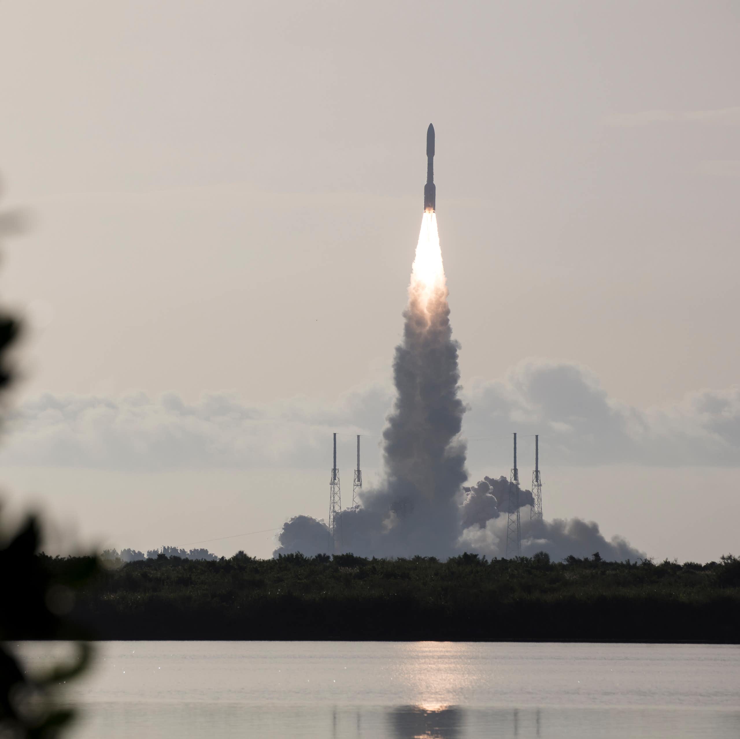 A rocket launching across a body of water, with a plume of smoke and flame coming from below it.
