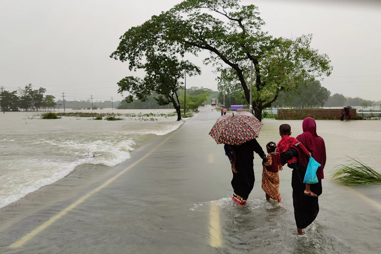 People with umbrellas in swollen river in Bangladesh.