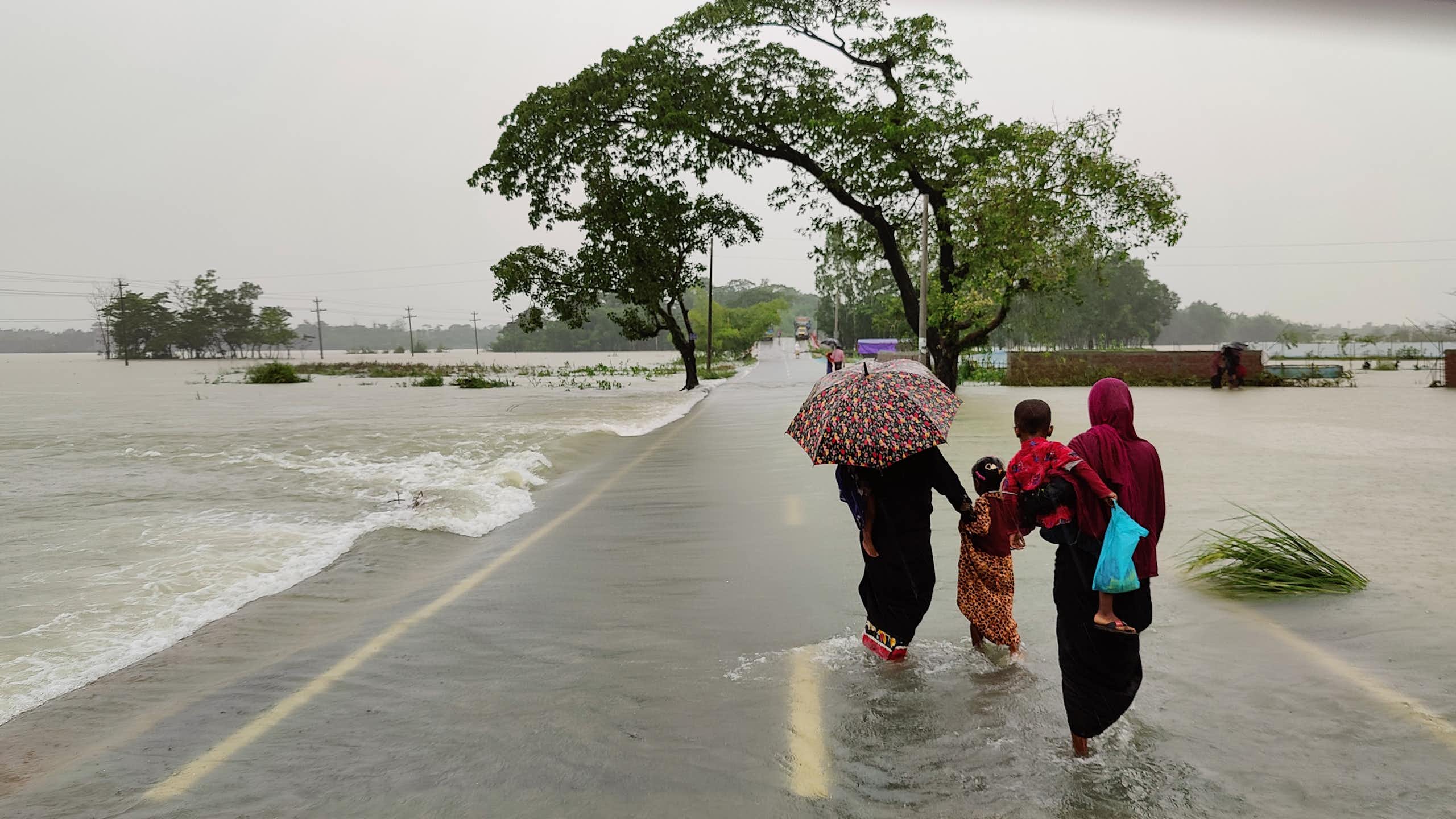 People with umbrellas in swollen river in Bangladesh.