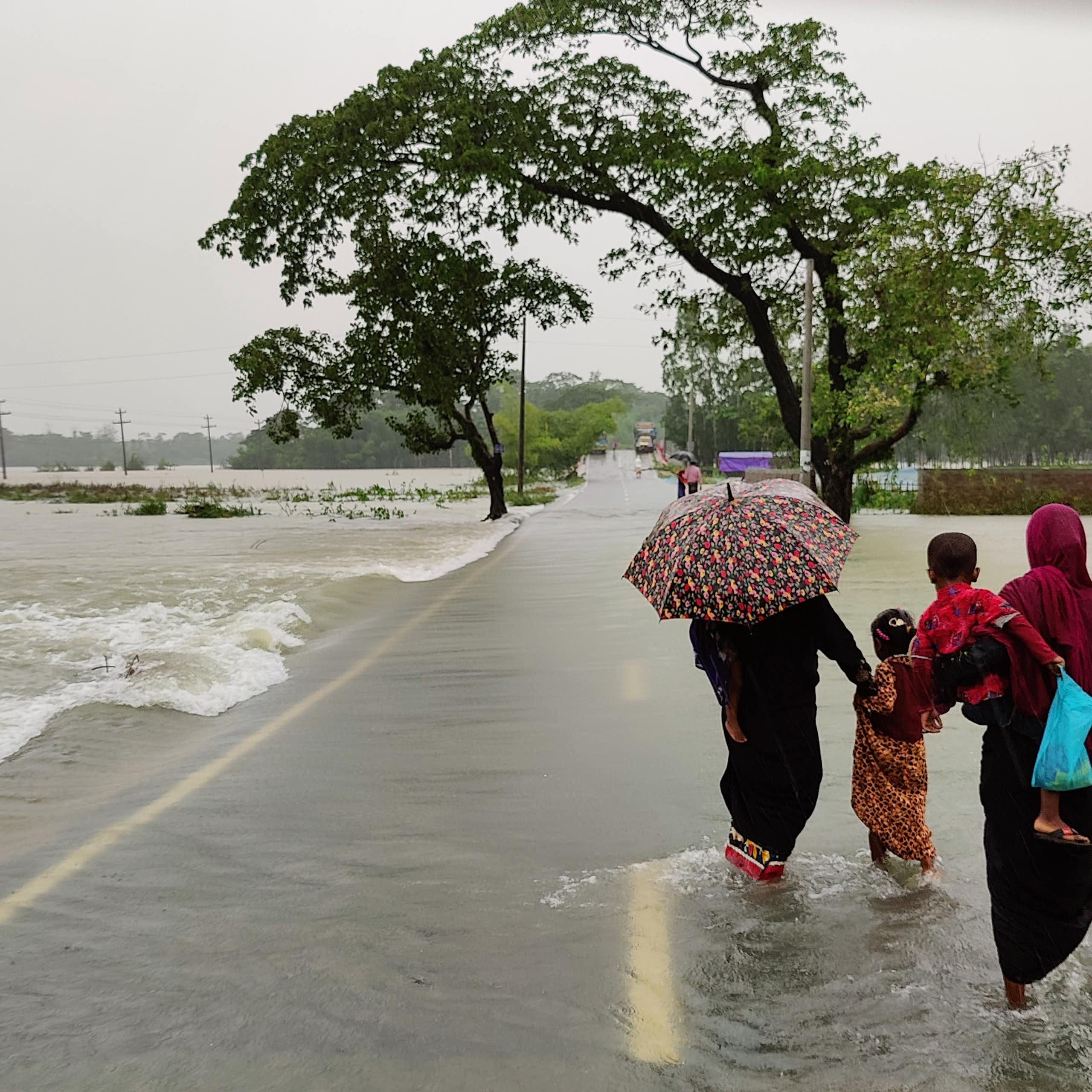 People with umbrellas in swollen river in Bangladesh.