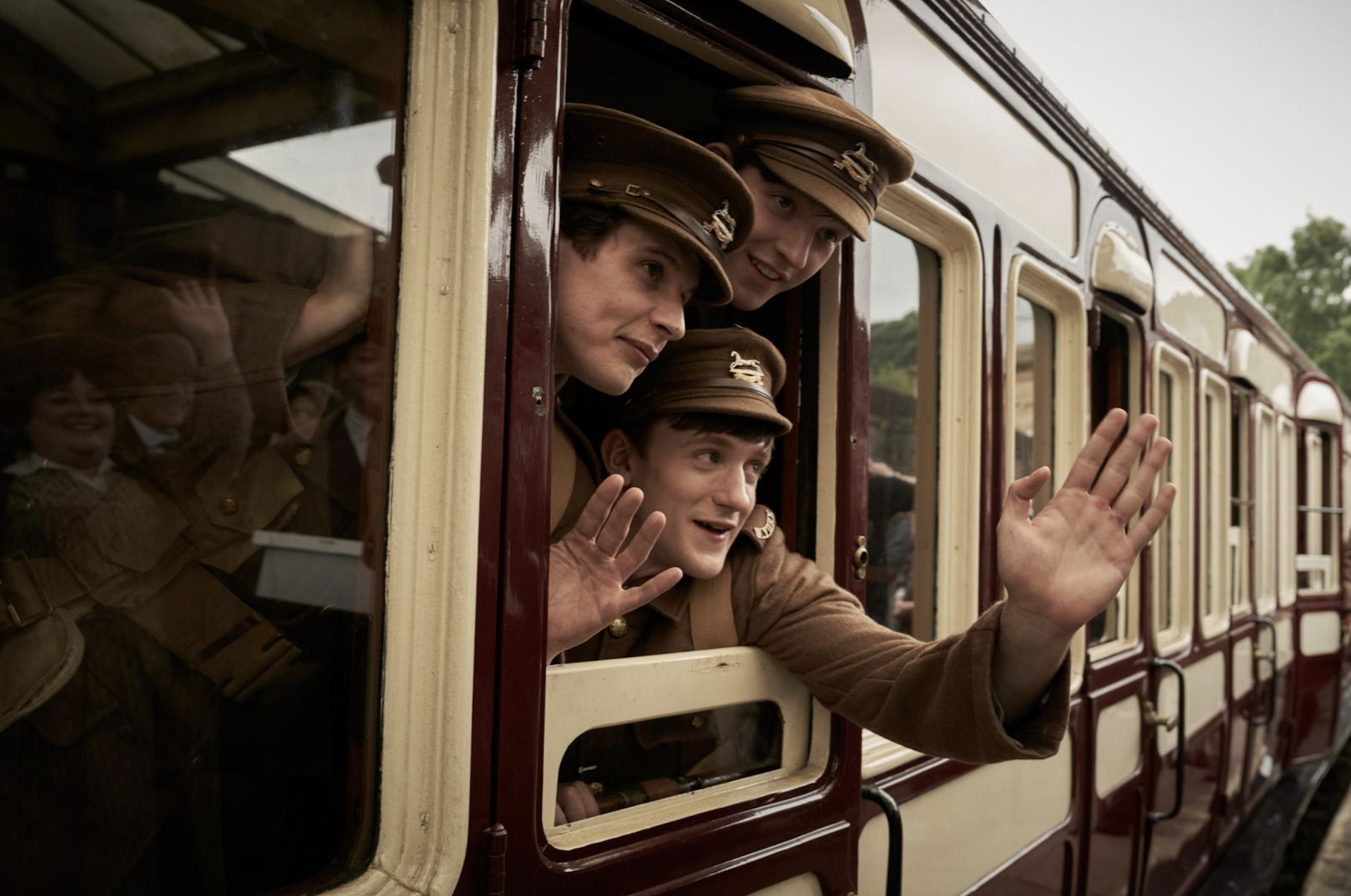 Young first world war soldiers in uniform waving from a train.