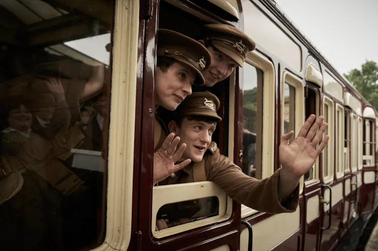 Young first world war soldiers in uniform waving from a train.