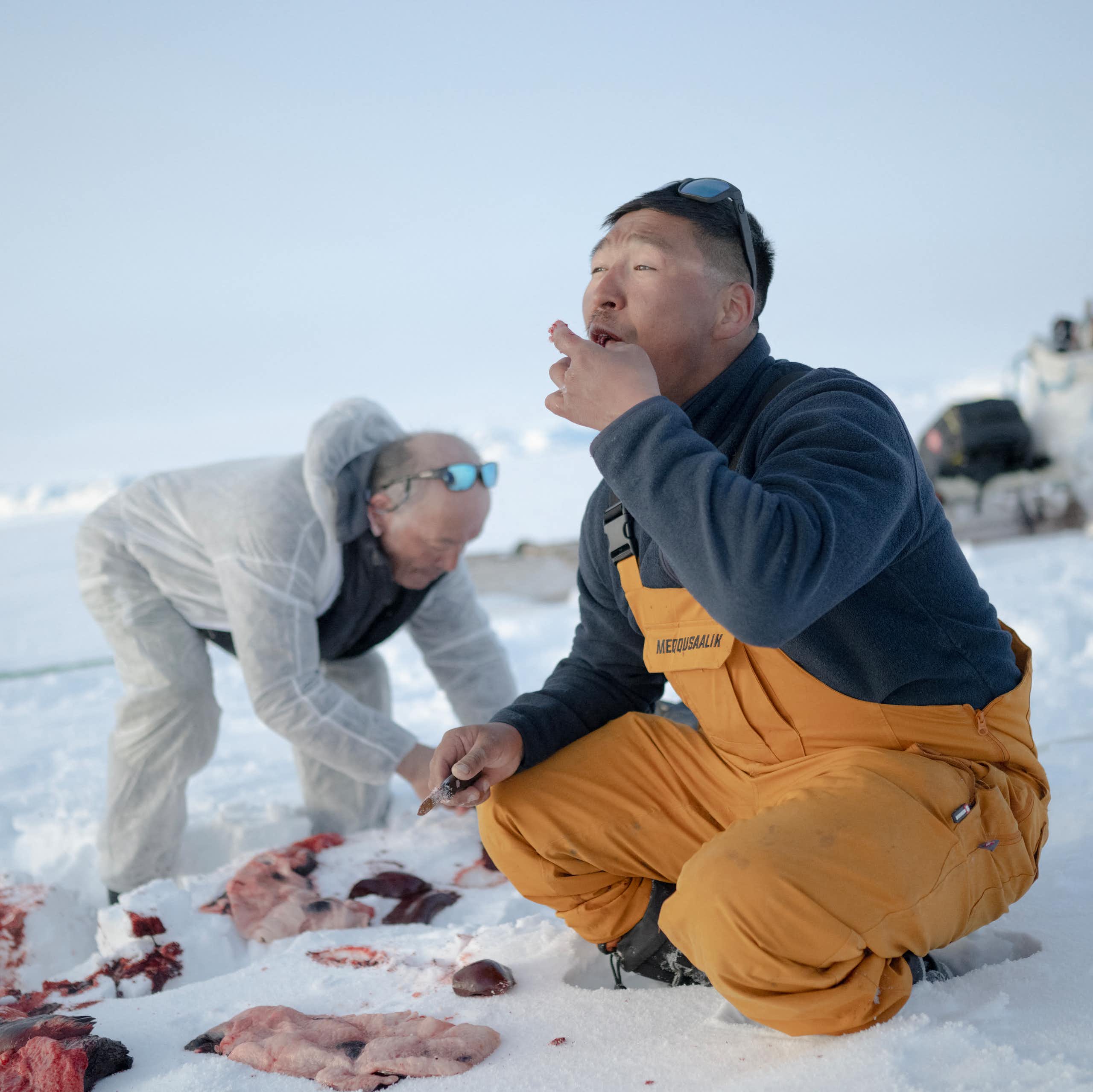two men on a snow-covered surface near the bloody remains of an animal