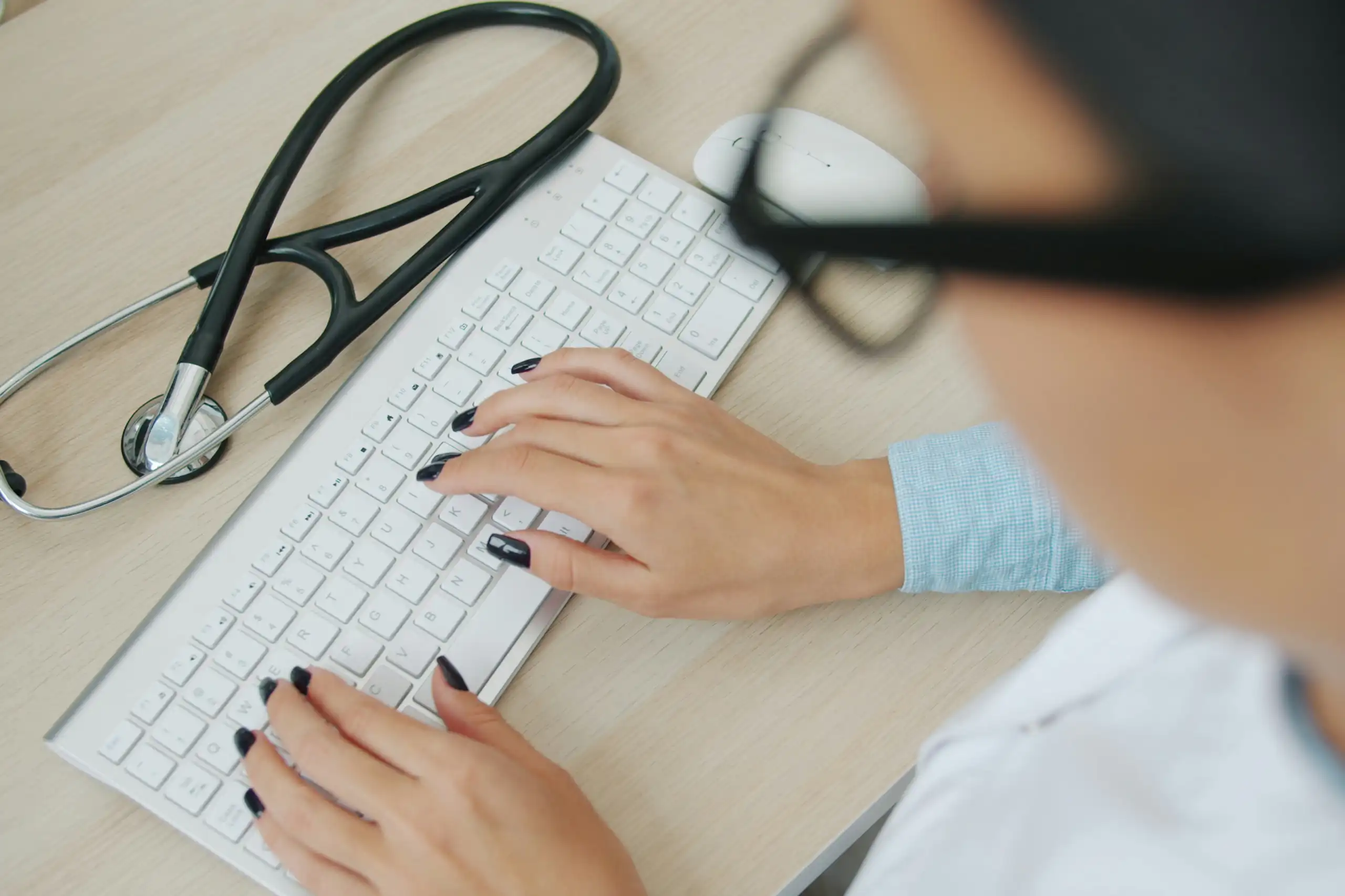 A person typing on a keyboard with a stethoscope on the desk