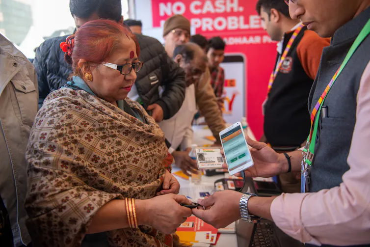 A woman in India scans her thumbprint on a device held by a man in a bank