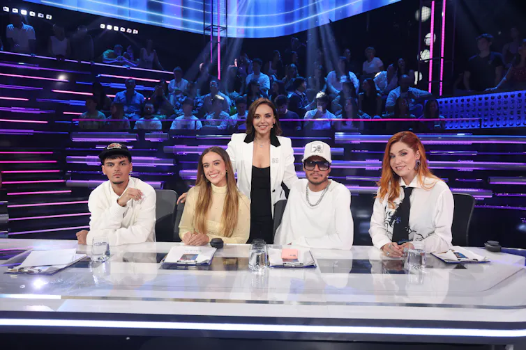 Cinco personas posan en una mesa en el escenario.