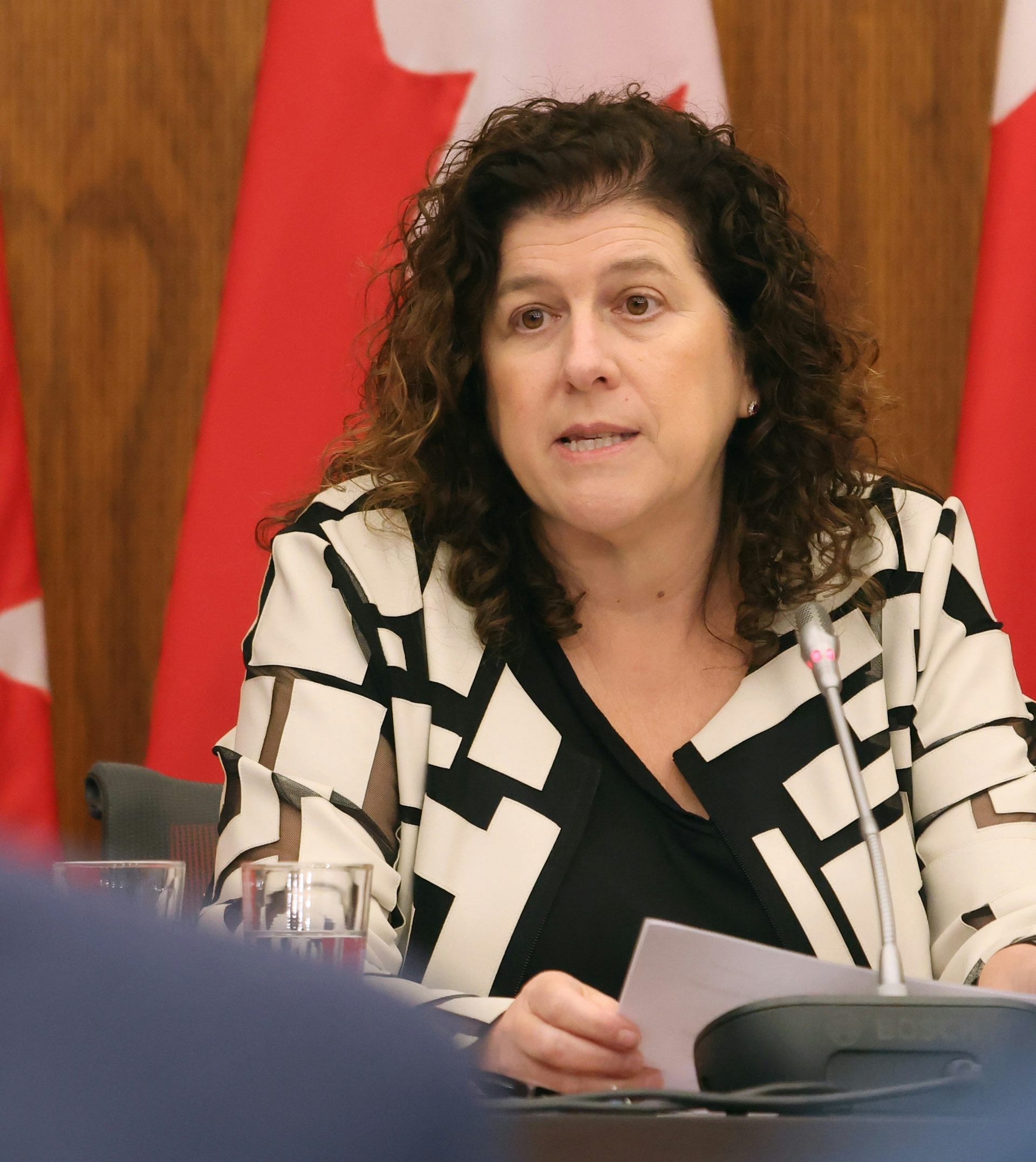 A woman at a table with a microphone and paper.