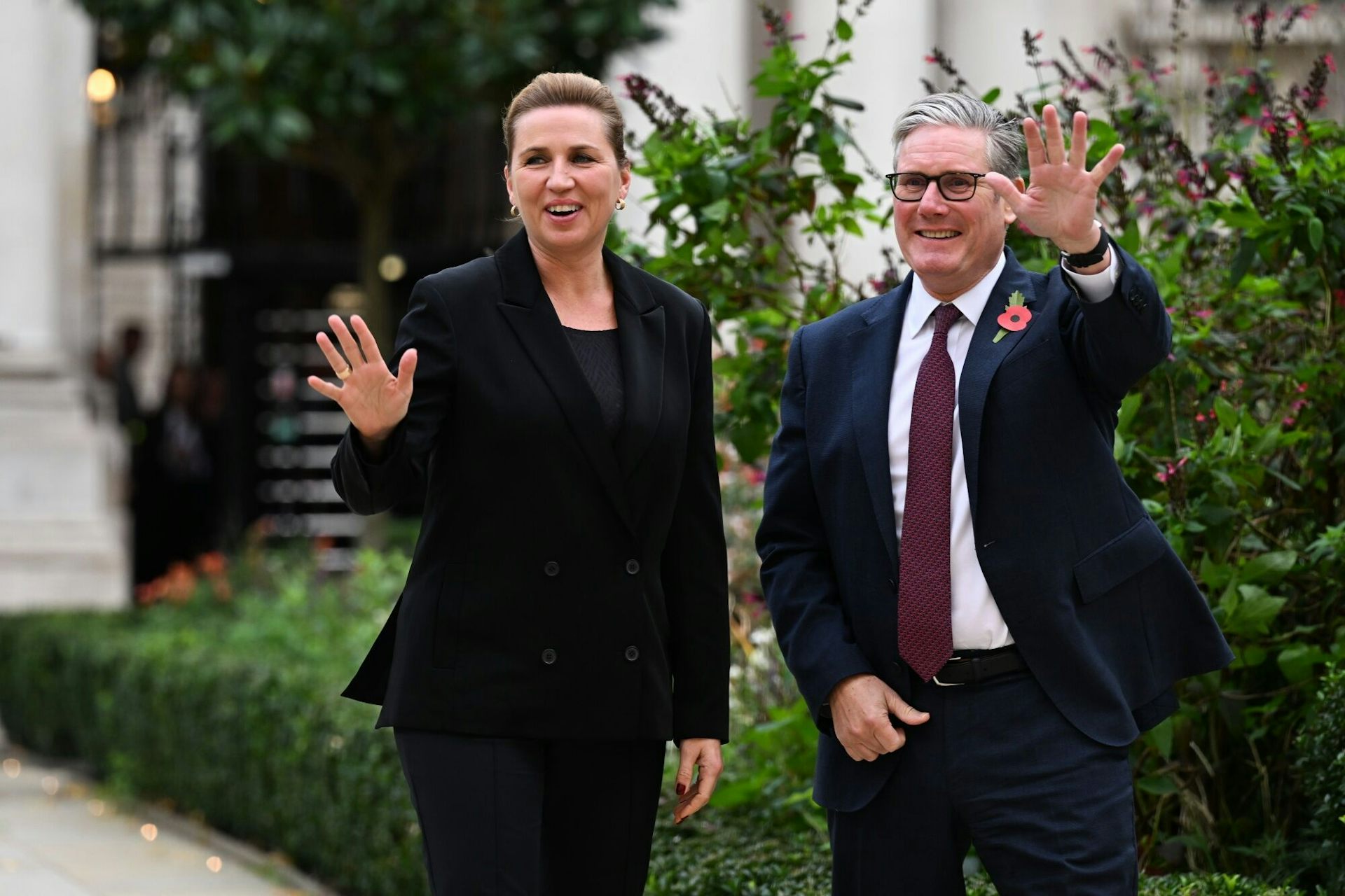 Frederiksen and Starmer walking side by side outdoors and waving at the camera