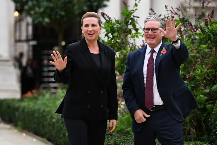 Frederiksen and Starmer walking side by side outdoors and waving at the camera