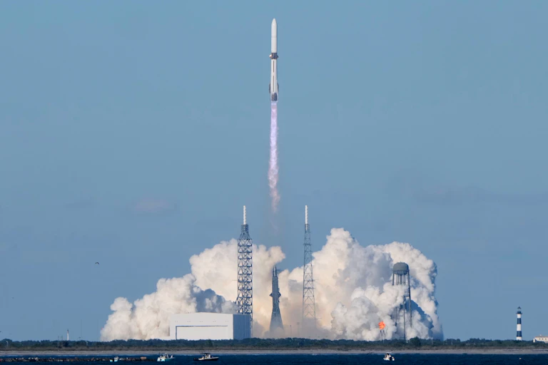 A long, thin rocket lifting off from a smoke-filled launchpad.