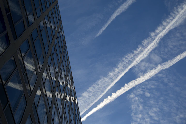 contrails against a blue sky and reflected in a large glass-front building