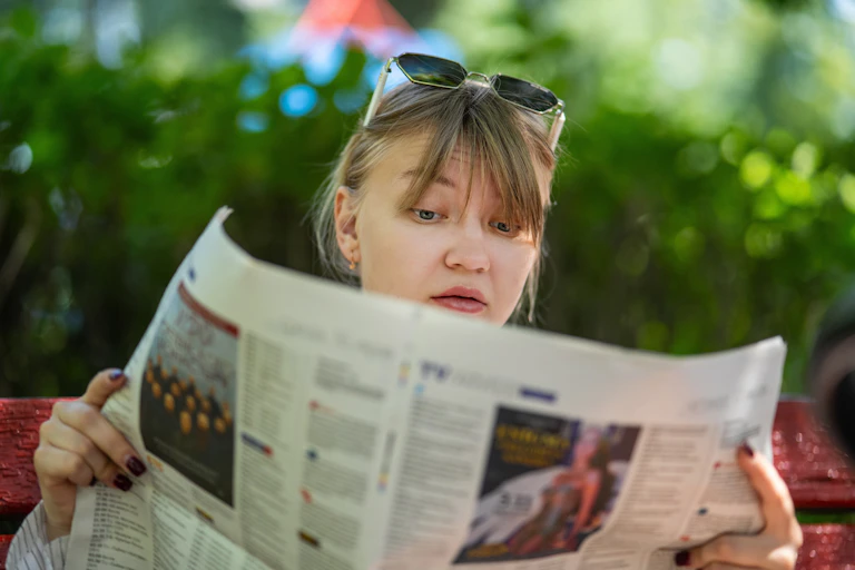 A young woman reading a newspaper with a surprised look on her face