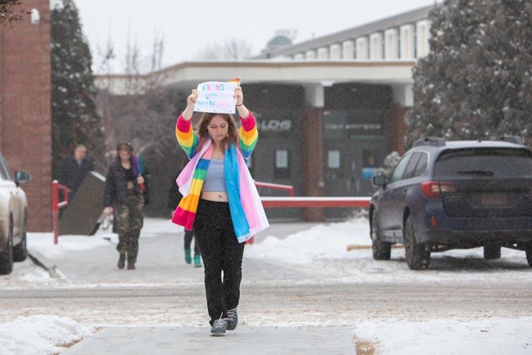 Un estudiante con un abrigo de arcoíris lleva un cartel.