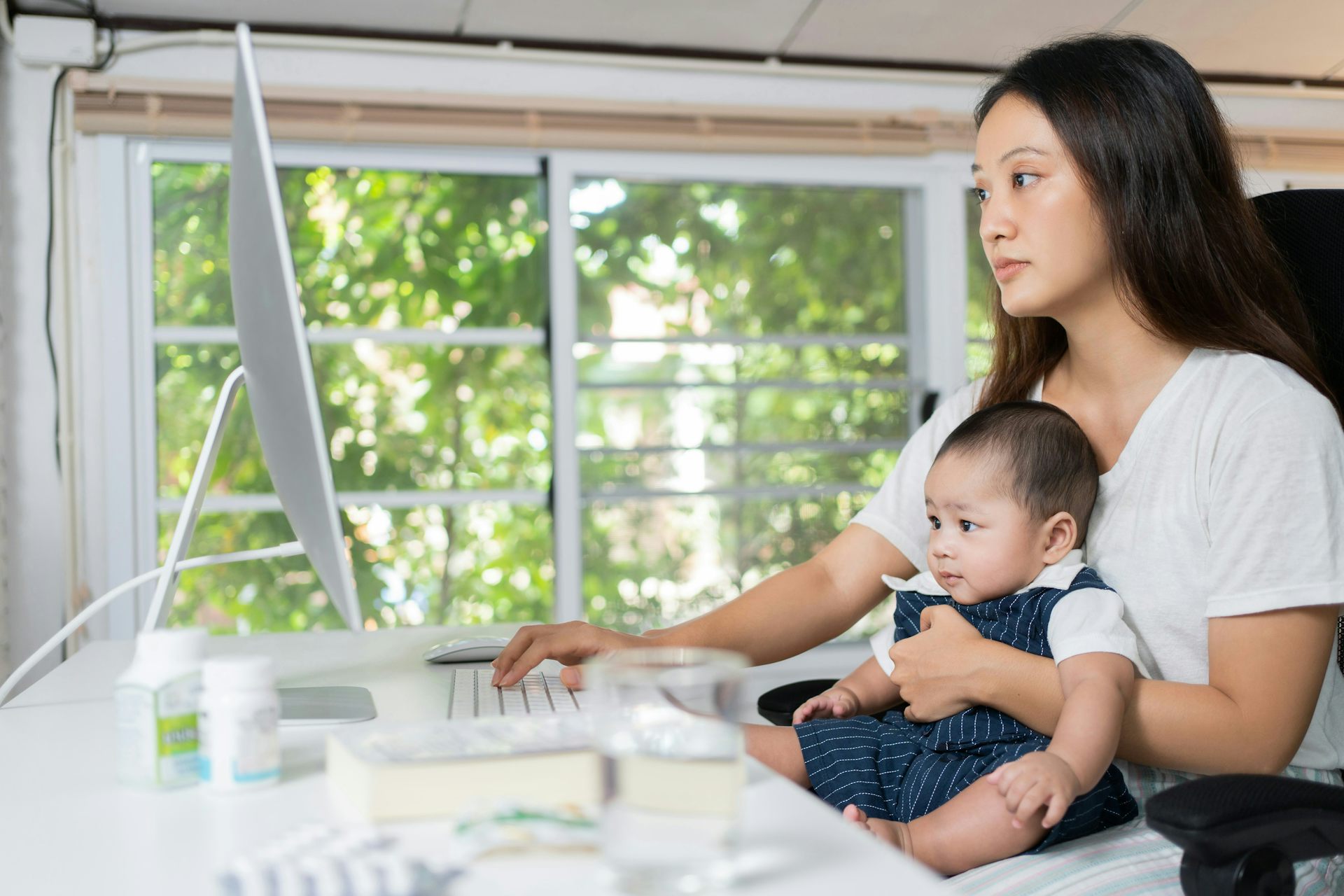 A woman in front of a computer and holding her baby.