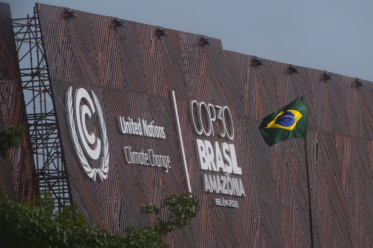 Una bandera brasileña en un poste al lado de un edificio con COP 30 Brasil escrito en letras grandes.