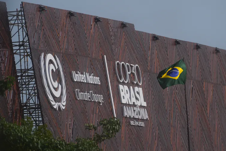 the flag of brazil on a pole next to a building with the words COP 30 Brasil written on it in large letters