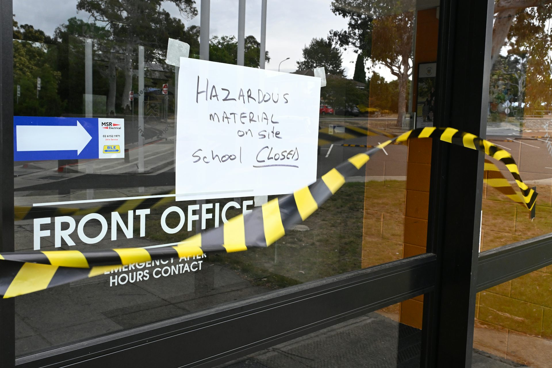 Hazard tape and a sign saying 'Hazardous material, school closed' on the door of a school's front office. 