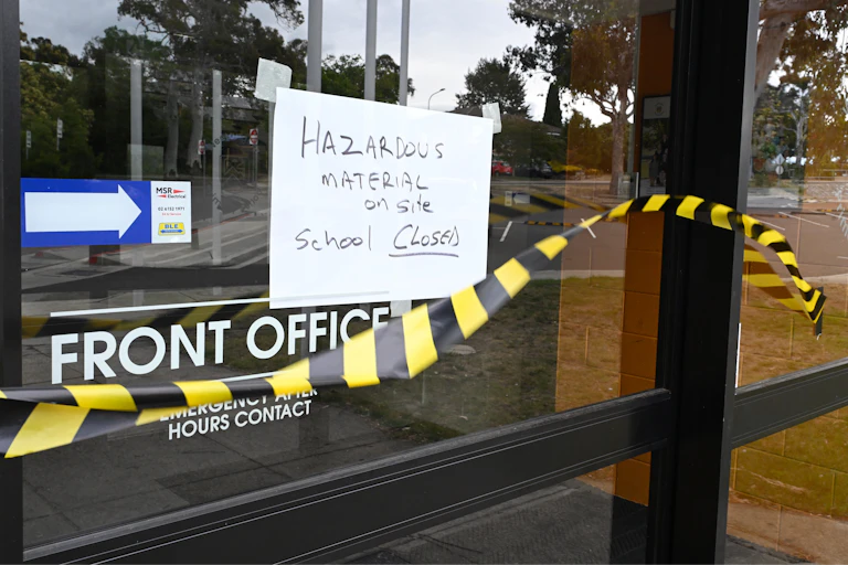 Hazard tape and a sign saying 'Hazardous material, school closed' on the door of a school's front office.