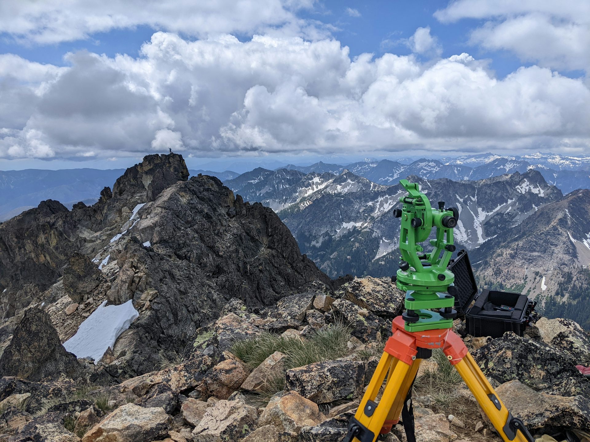 A greean machine with yellow tripod legs sits on a mountain top.