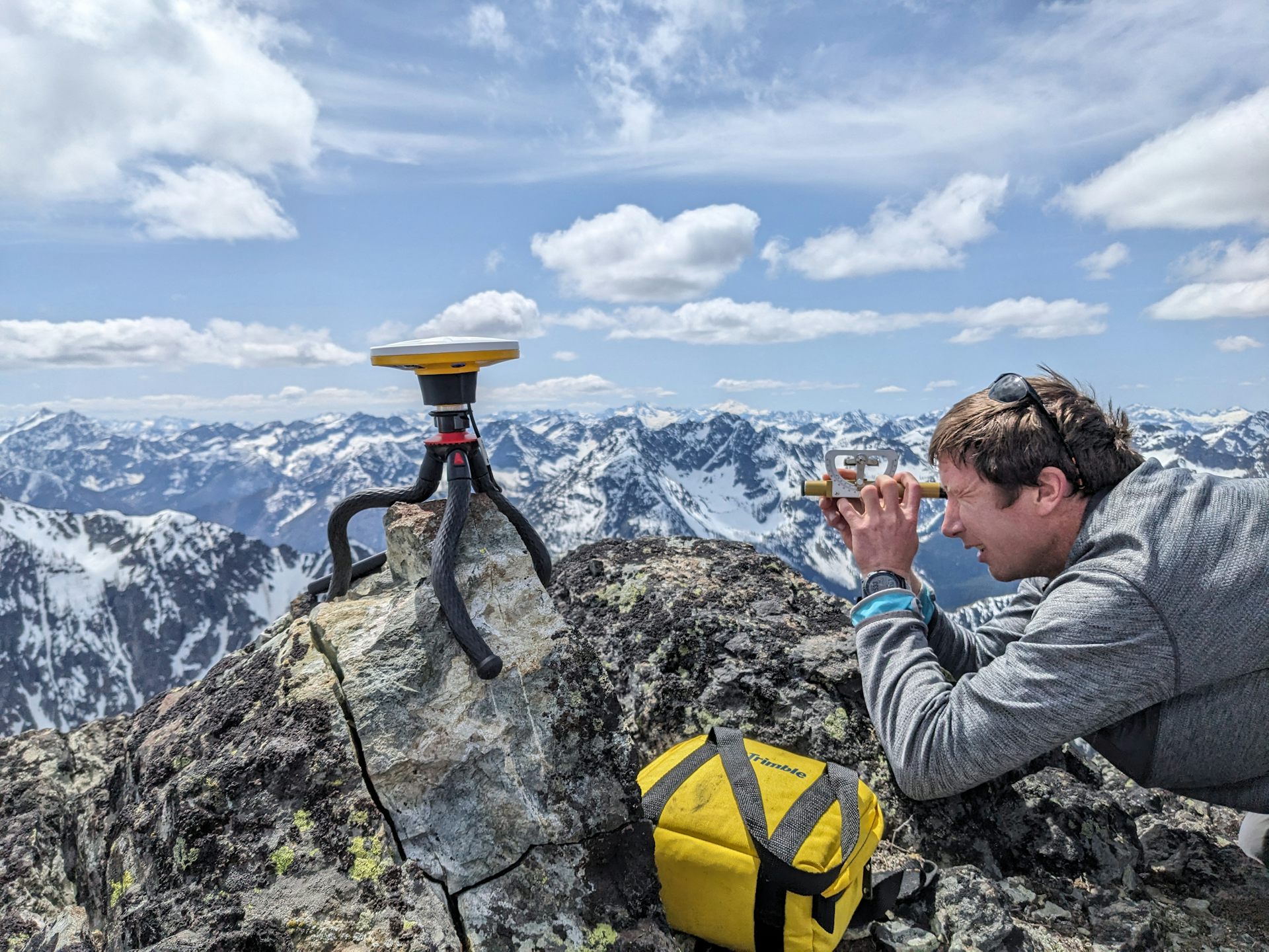 A small flat instrument sits on a tripod near a man who holds a measuring device to his eyes.