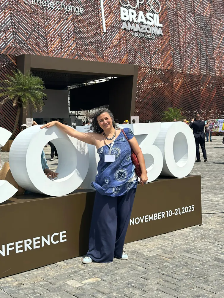 woman in bluie blothes standing by COP30 sign outside building