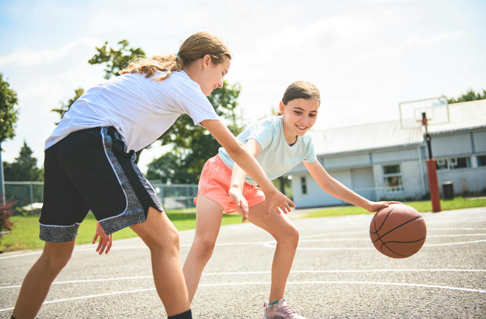 Two girls play basketball outside.