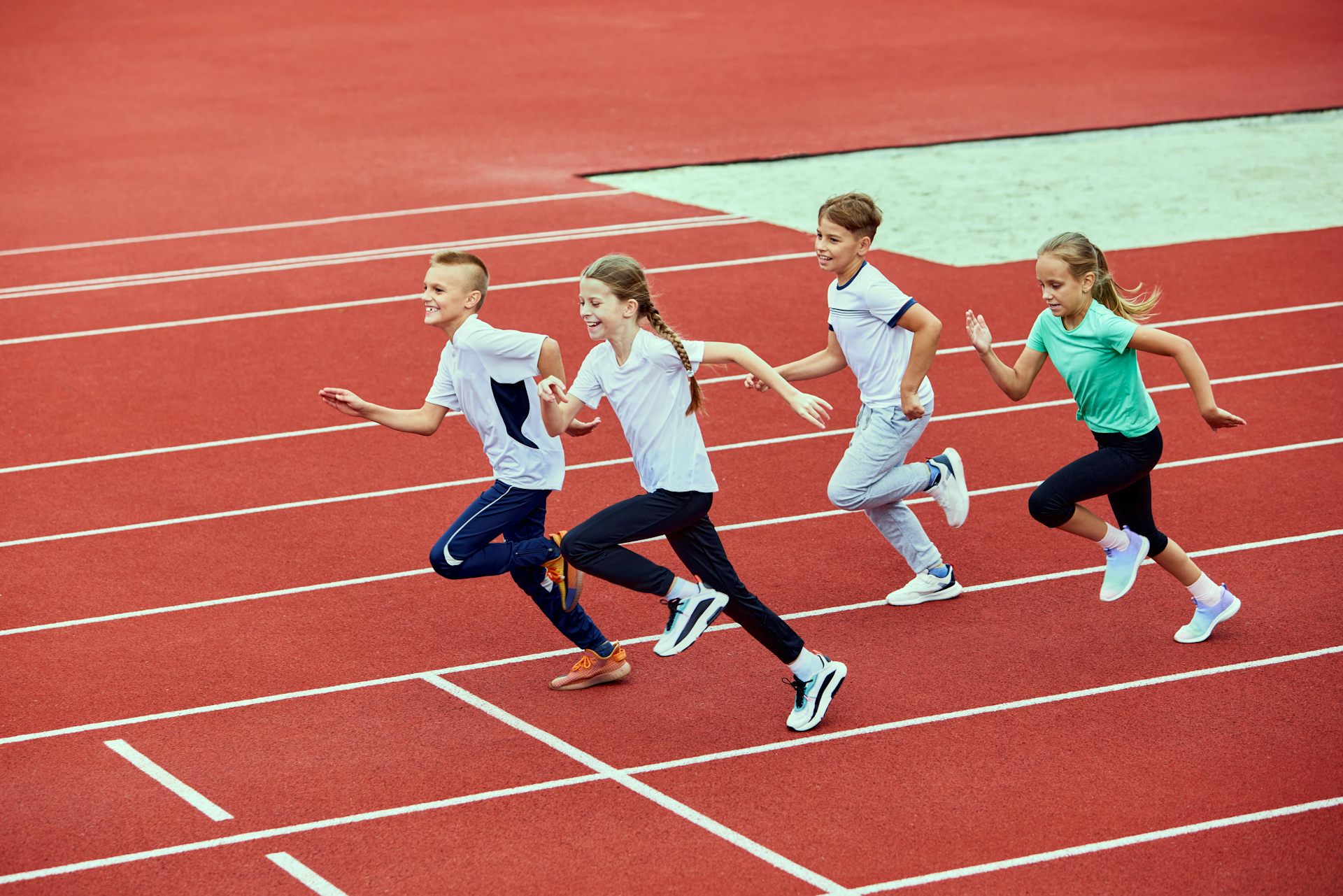 Four children running on an outdoor track.