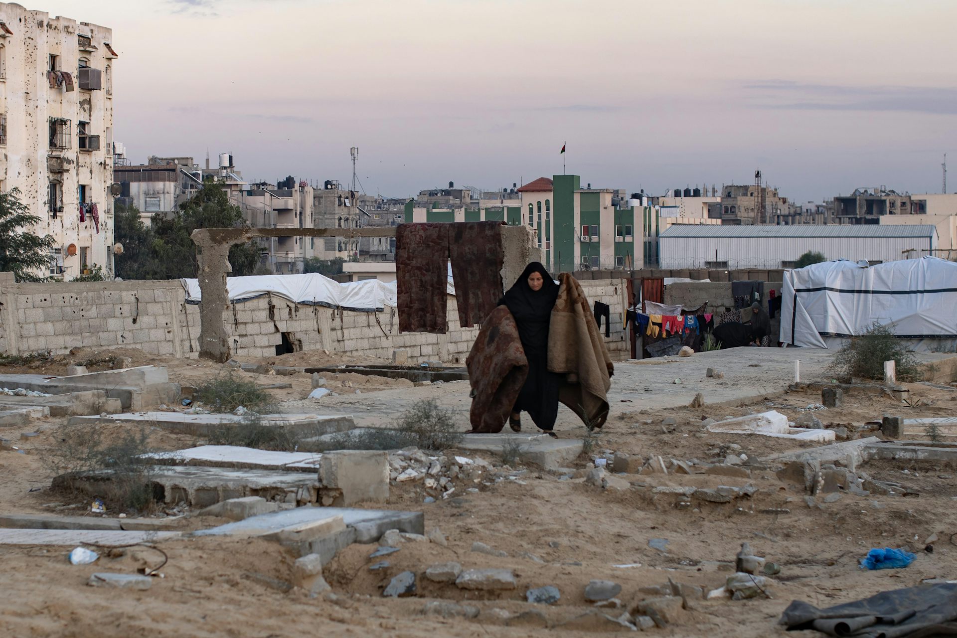 A Palestinian woman holds up carpets in a cemetery in Gaza.