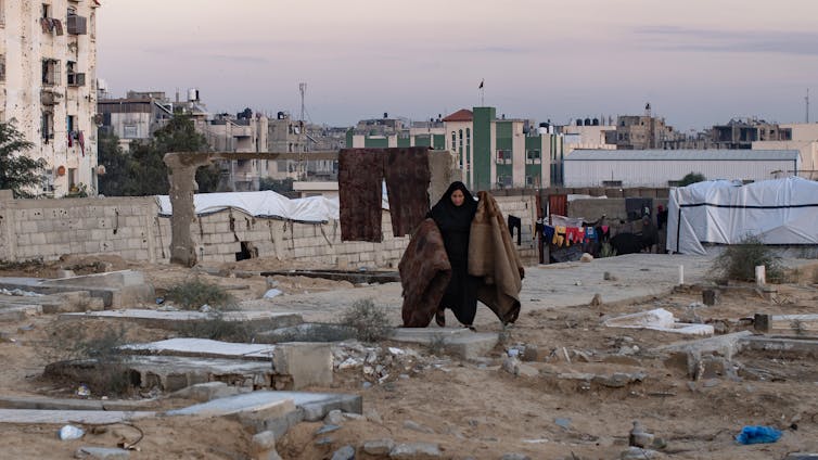 A Palestinian woman holds up carpets in a cemetery in Gaza.