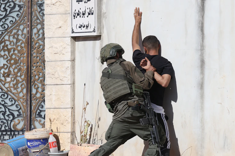 AN IDF soldier pushes a Palestinian man up against a wall in the West Bank.