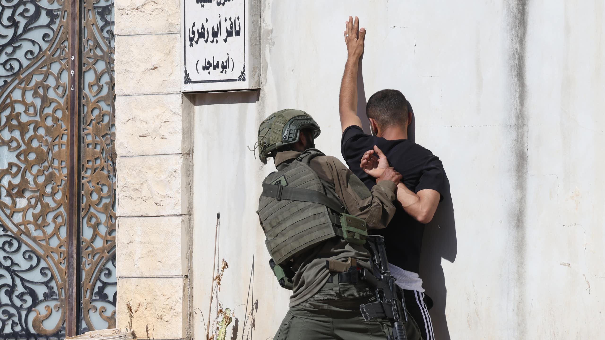 AN IDF soldier pushes a Palestinian man up against a wall in the West Bank.