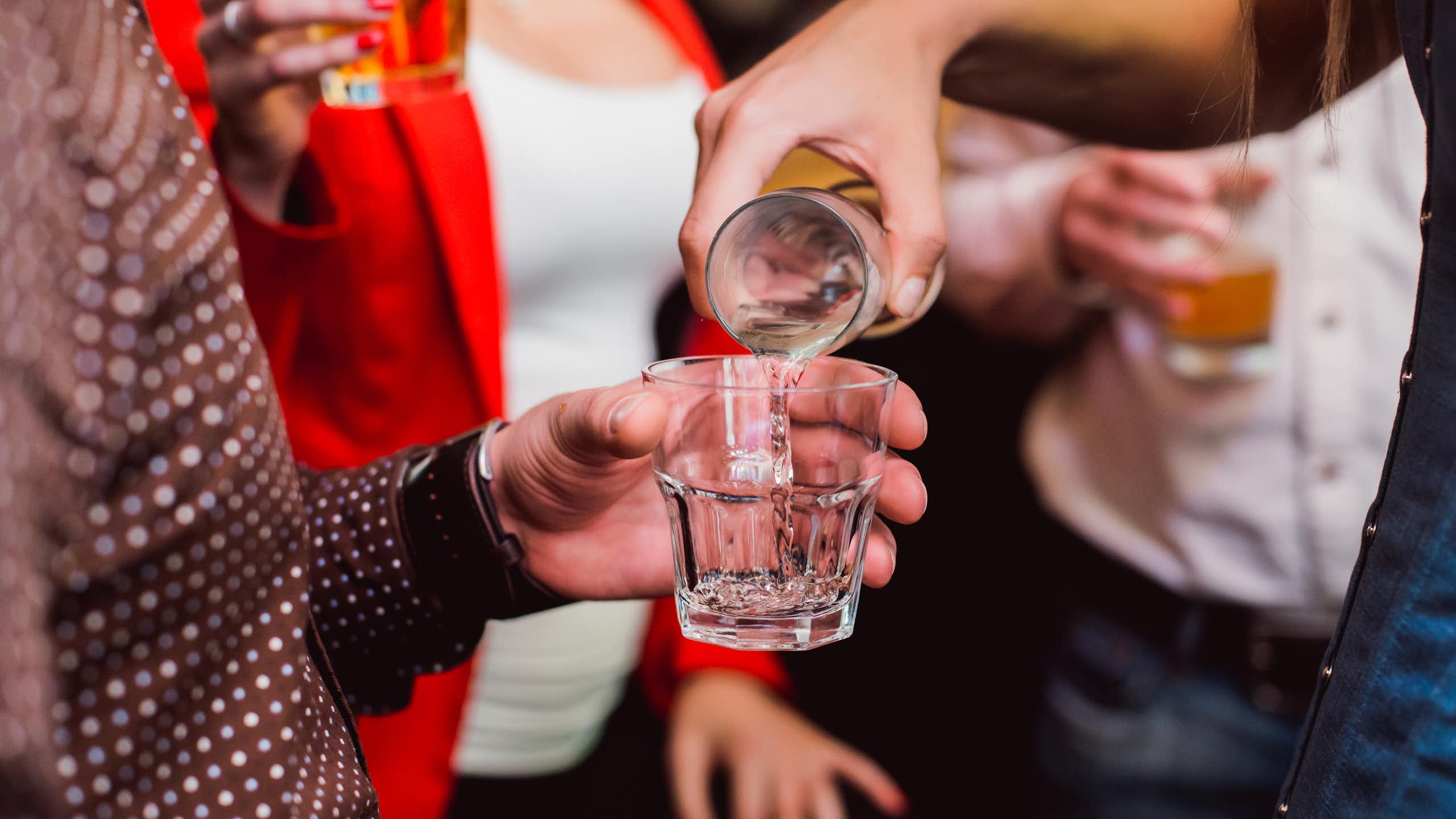 Un groupe de personnes en train de boire de l’alcool. Une femme reverse une boisson dans le verre de quelqu’un d'autre.