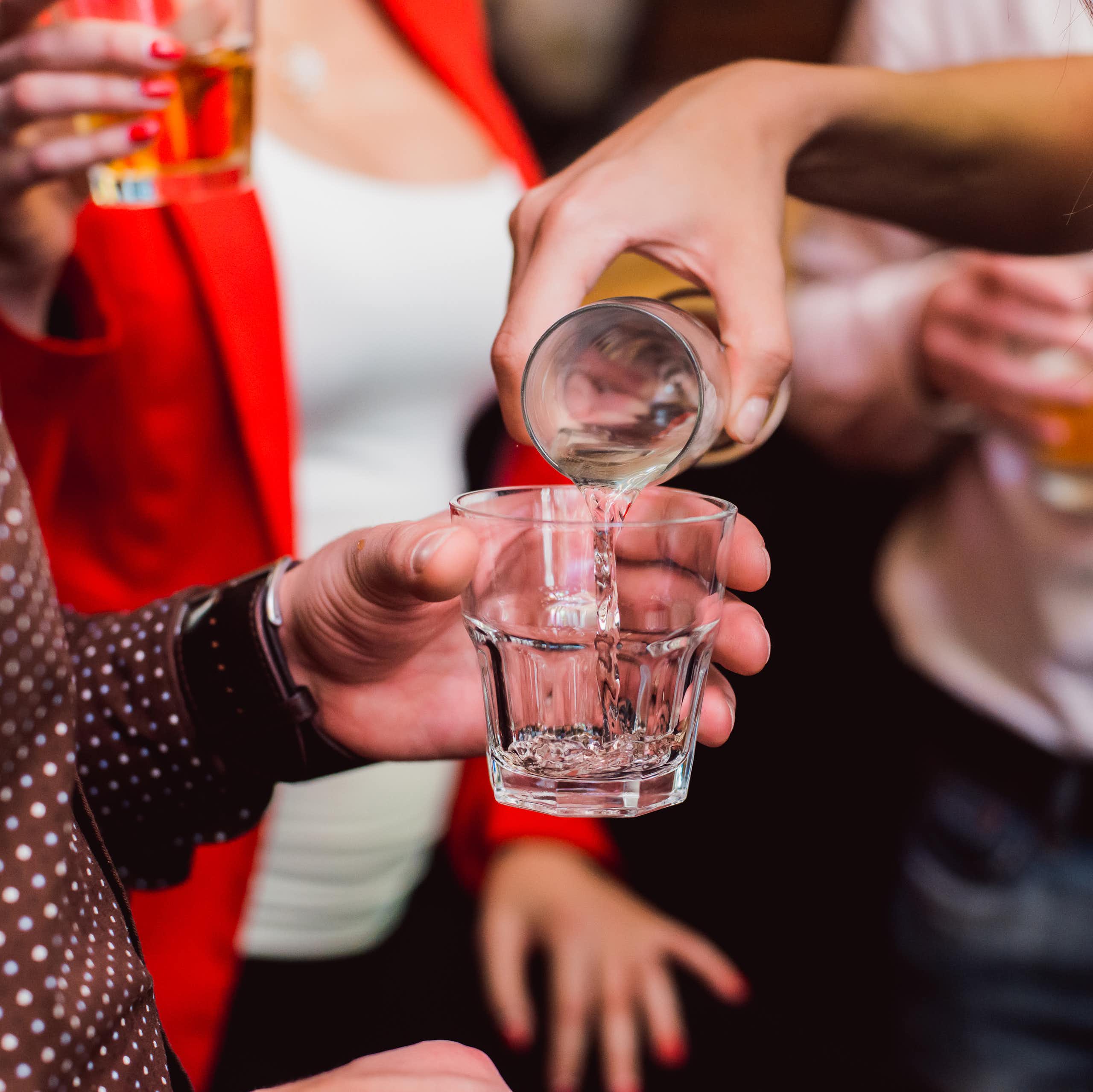 Un groupe de personnes en train de boire de l’alcool. Une femme reverse une boisson dans le verre de quelqu’un d'autre.