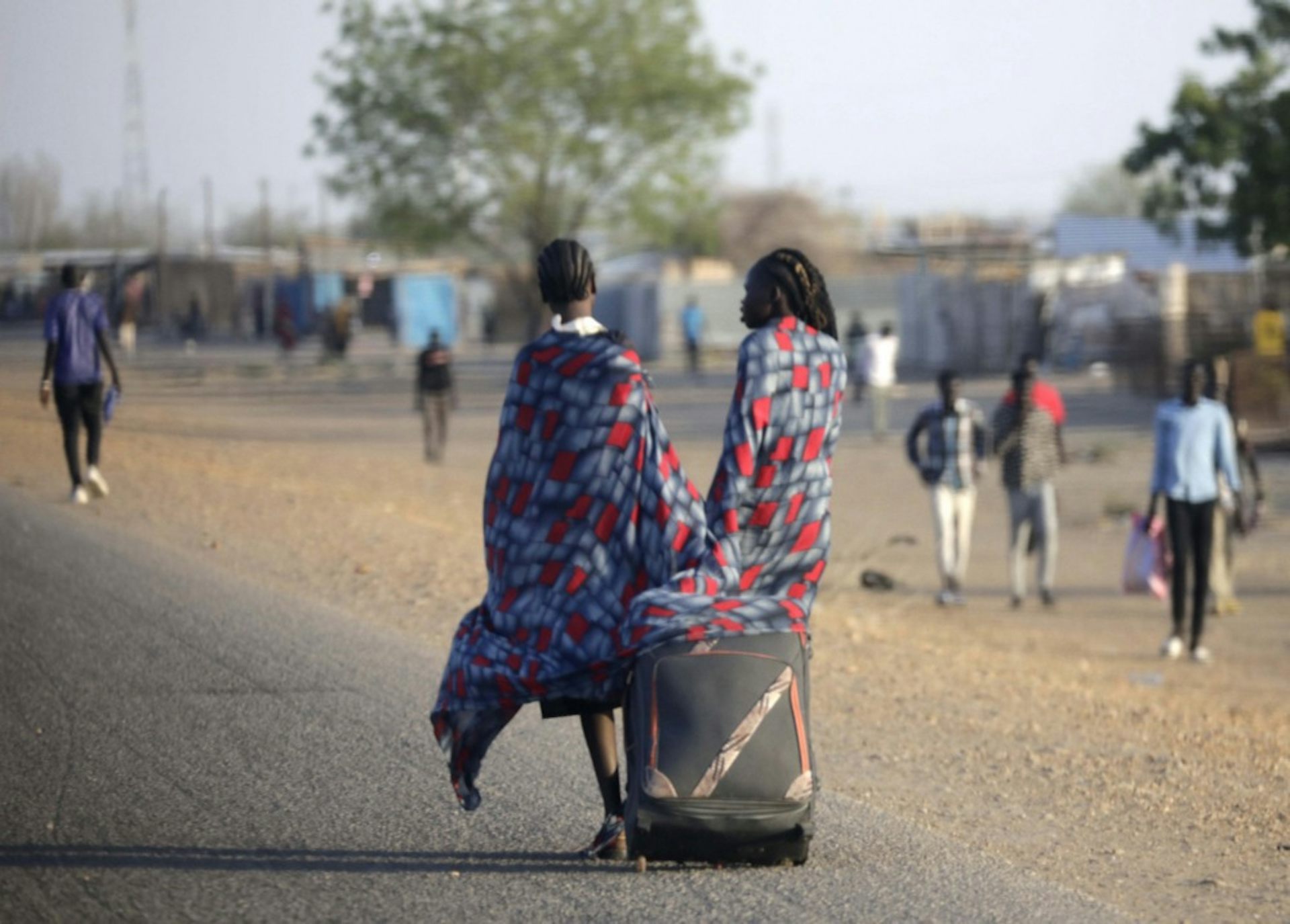 Two women pull a suitcase down a road.