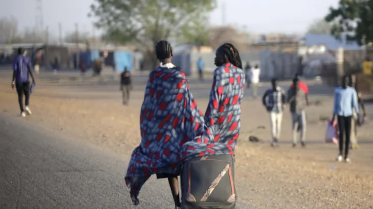 Two women pull a suitcase down a road.
