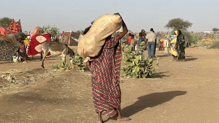 A woman carries a large sack on her back as she walks up a road.