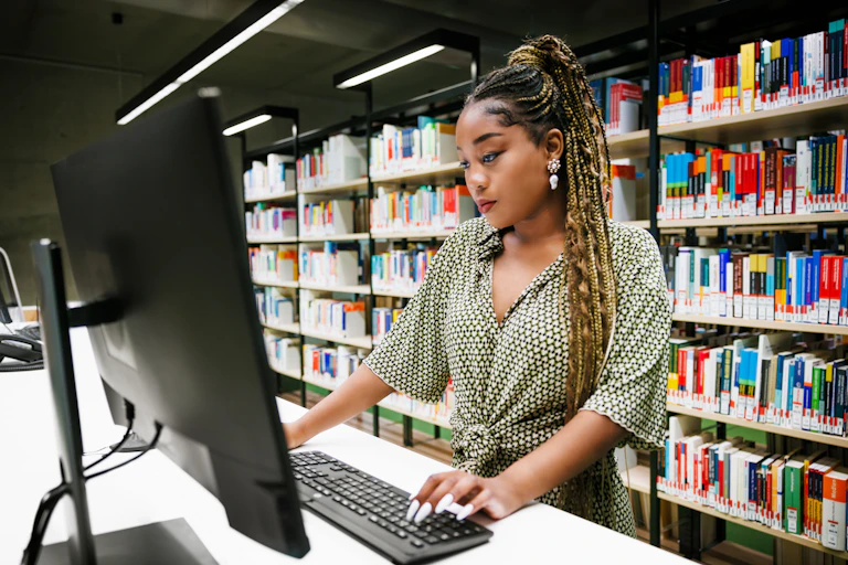 A woman doing research at a computer in a library.