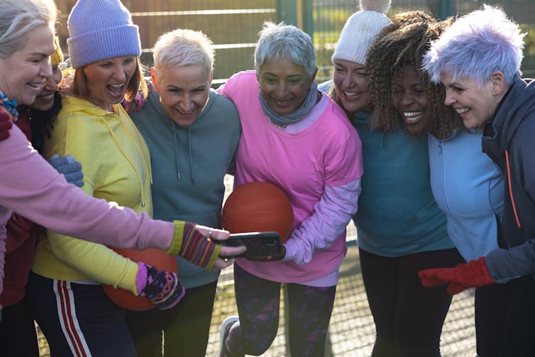 Las mujeres maduras en un frío día de verano se toman un descanso de los deportes para mirar una foto por teléfono.