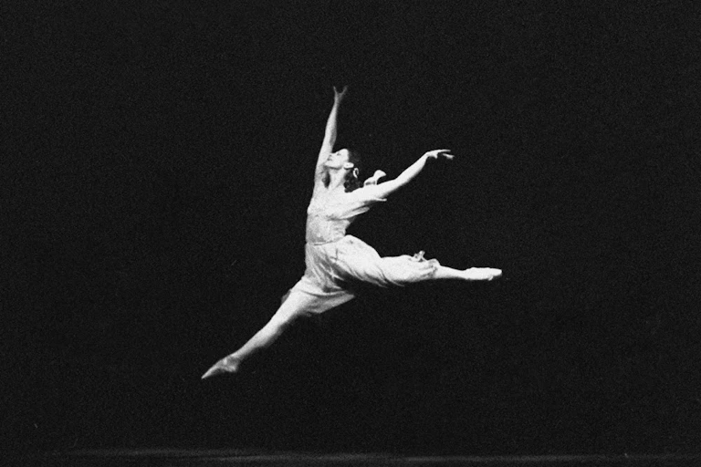 Fotografía de una mujer de blanco saltando y bailando sobre un fondo negro.