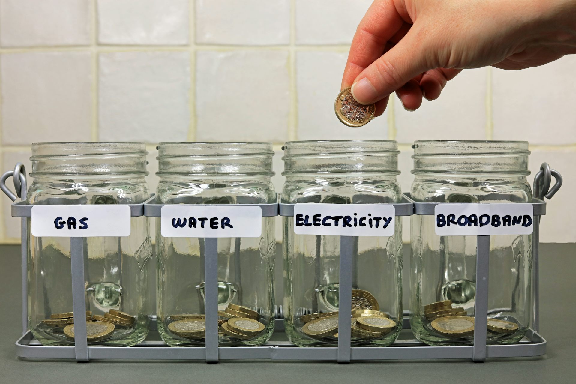 row of jars labelled with different household utilities, hand dropping a coin into the electricity jar