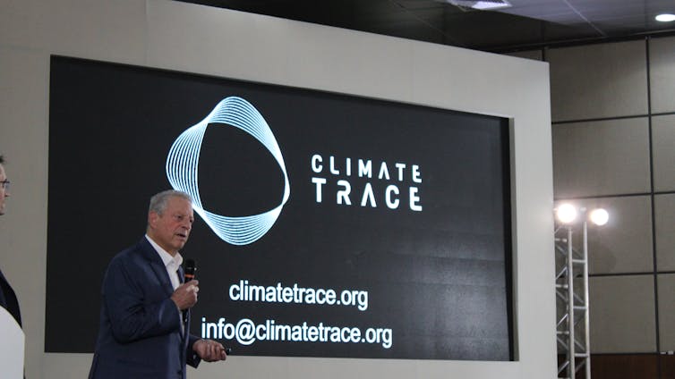 Un hombre con traje oscuro se encuentra frente a una gran pantalla que muestra las palabras Climate Trace.