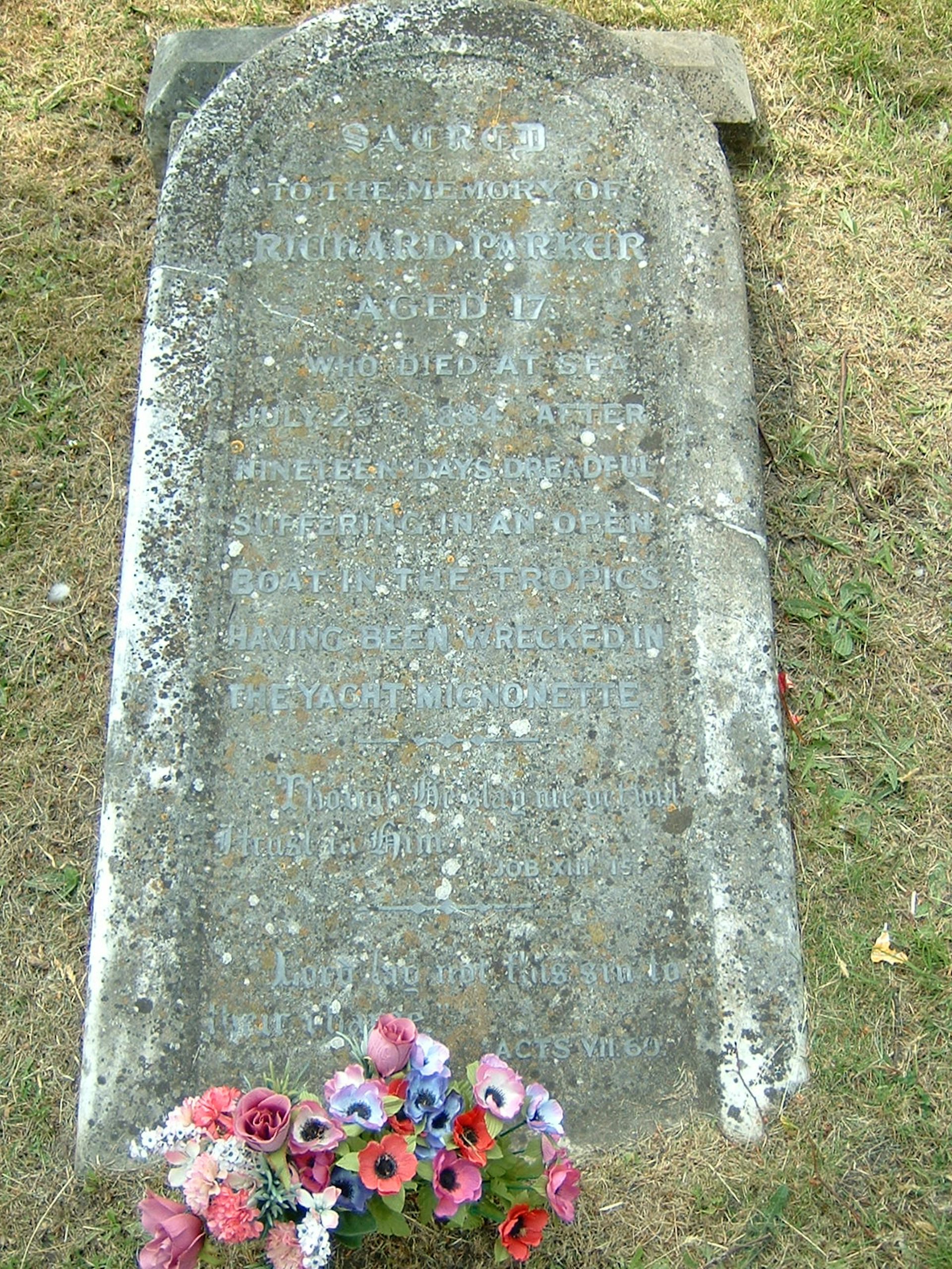 A faded tombstone lying on the ground with a bouquet of pink flowers at the base.