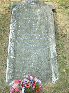 Una lápida descolorida tirada en el suelo con un ramo de flores rosas en la base.