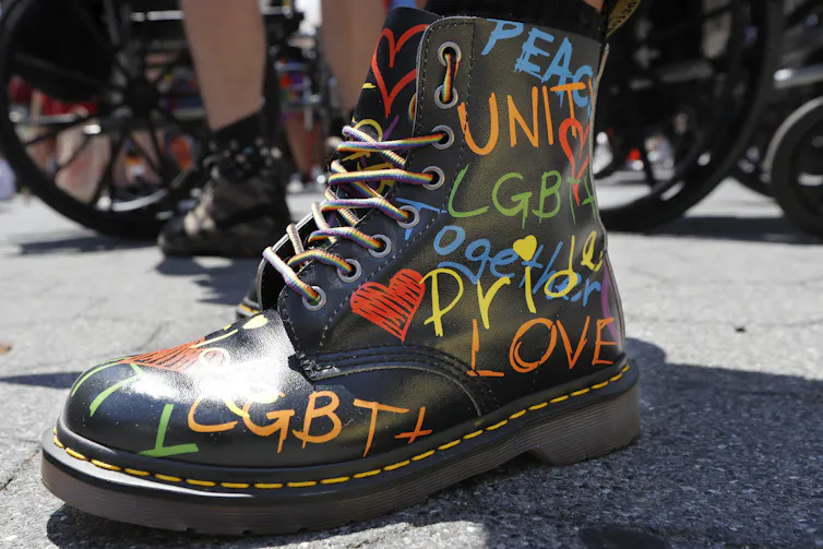 Une botte noire sur laquelle sont inscrits des mots liés à la communauté LGBTQ et à la fierté avec un marqueur arc-en-ciel