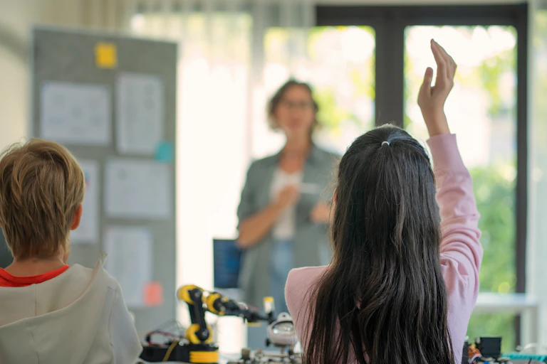 Rear viewpoint of school students raising their hands to answer the teacher's question in a science class