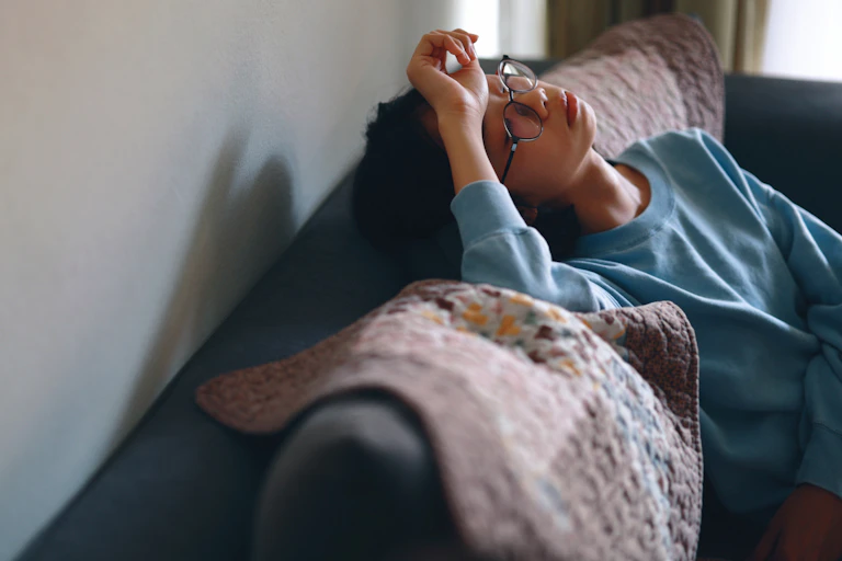 Person sitting on couch with head tilted back, hand on forehead