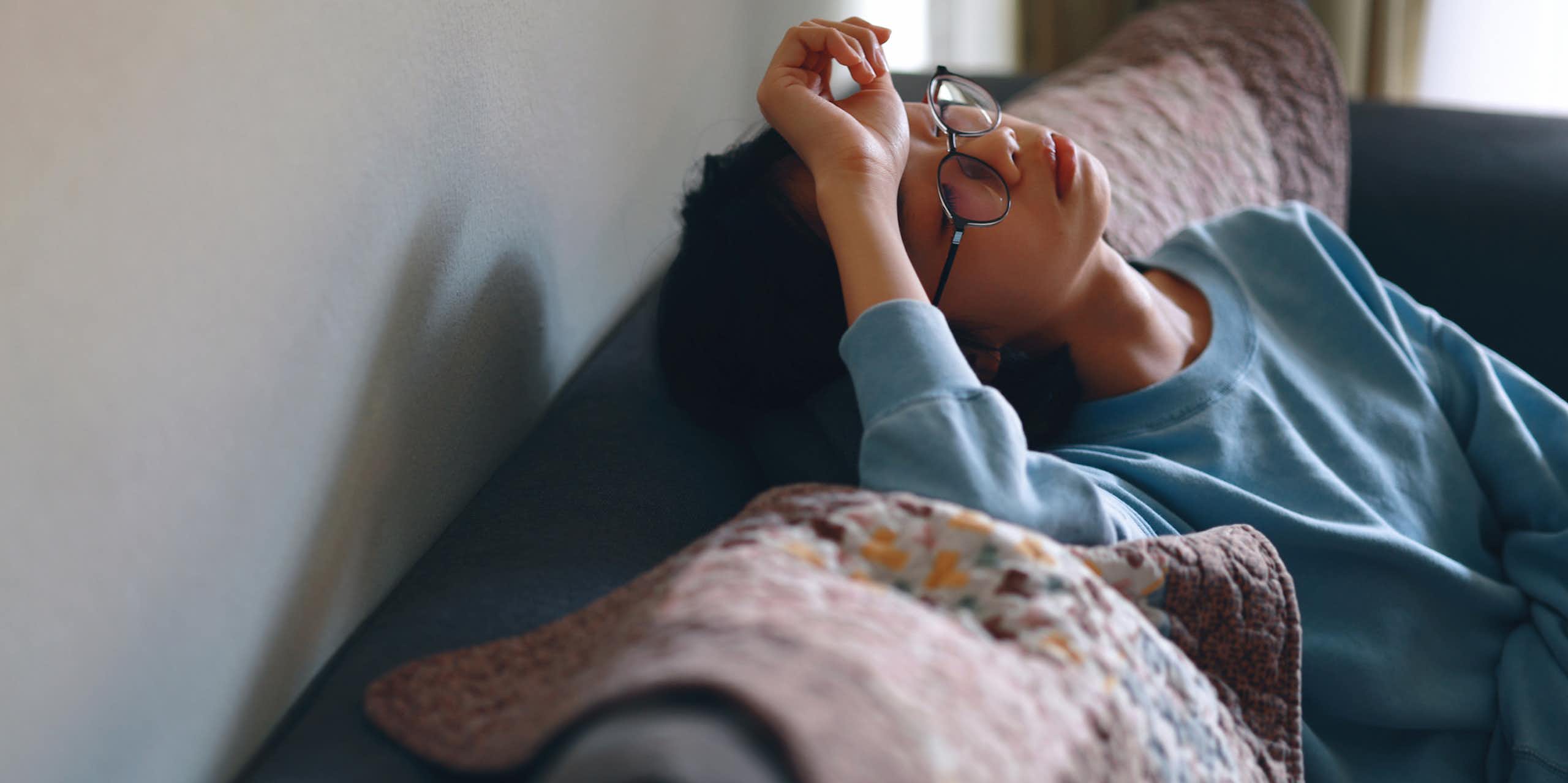 Person sitting on couch with head tilted back, hand on forehead