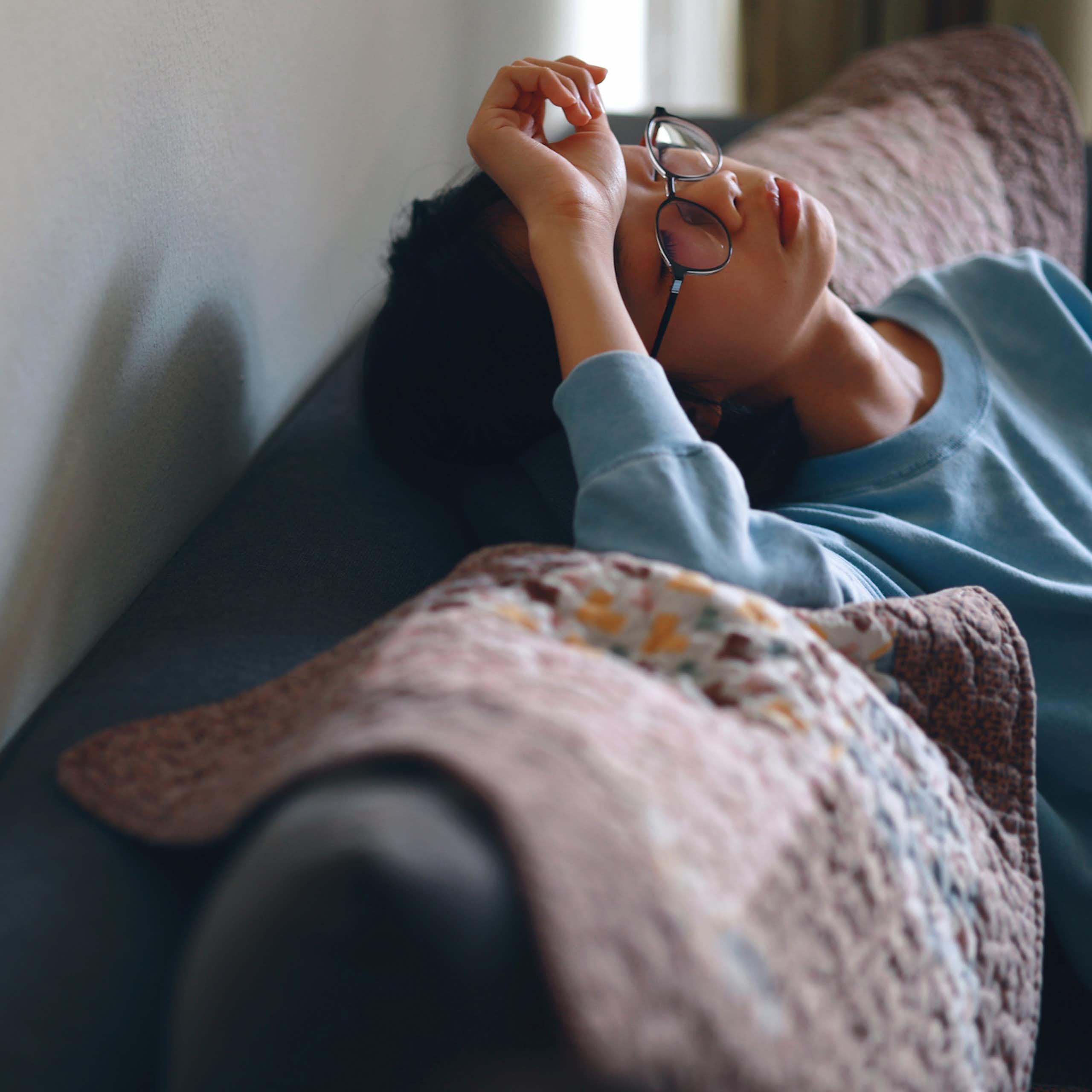 Person sitting on couch with head tilted back, hand on forehead