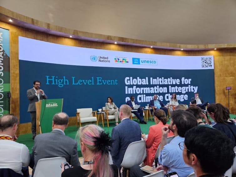 un hombre en un podio habla ante una audiencia sentada. un gran cartel detrás dice: Iniciativa Global para la Integridad de la Información sobre el Cambio Climático.