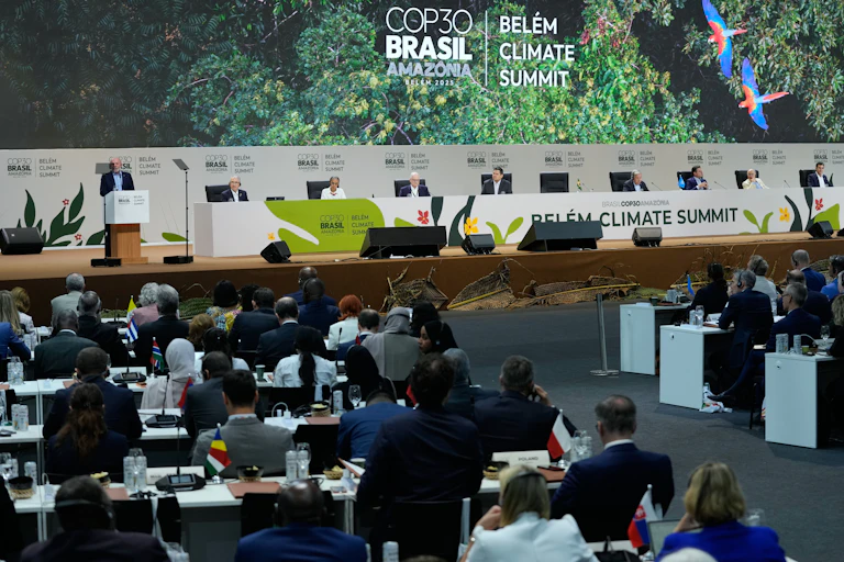 people attend a convention in a large hall. COP30 Brasil is written in large letters on the wall behind a dais